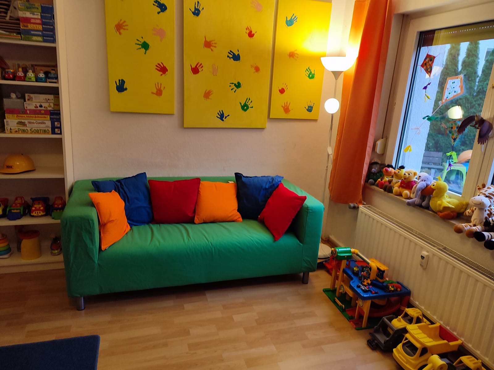 Gemütliche Spielecke mit grünem Sofa, bunten Kissen und Handabdruck-Bildern