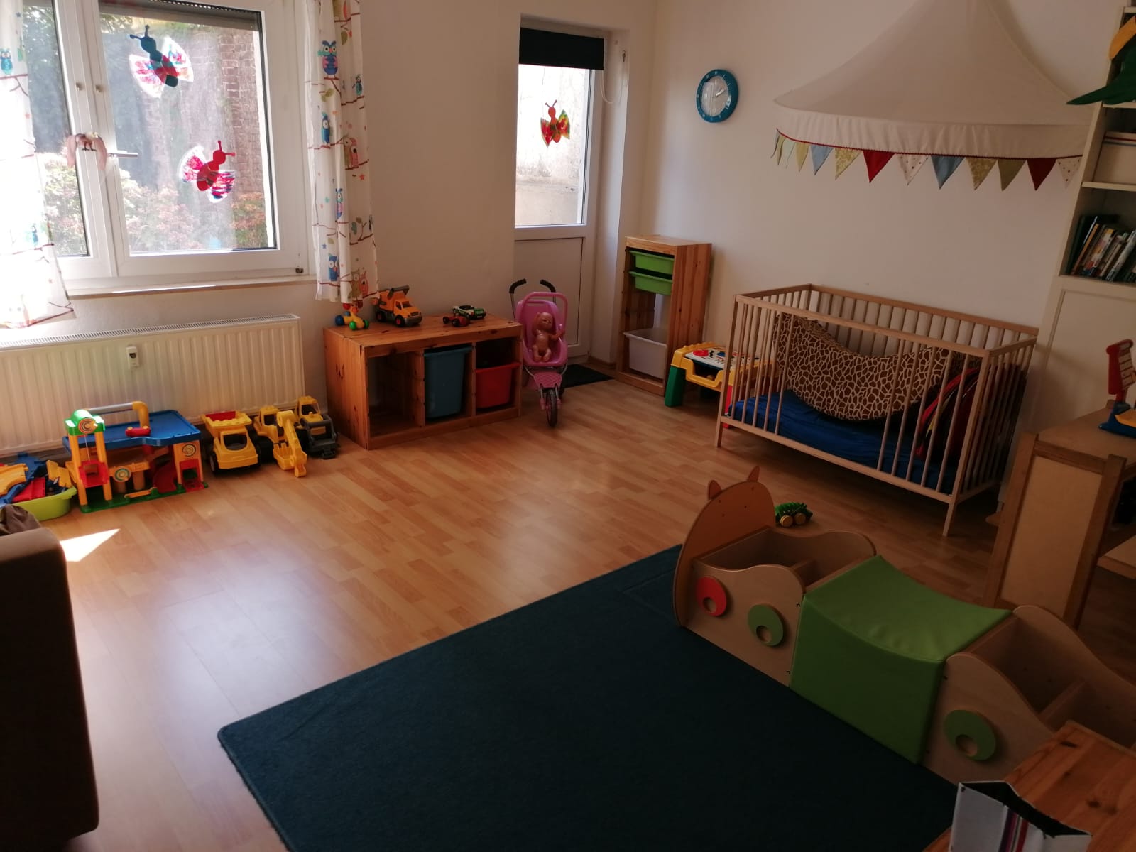 Heller Gruppenraum mit Spielzeug, Babybetten und großem Fenster